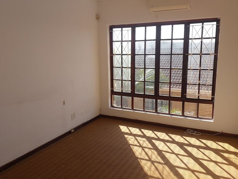 An empty bedroom featuring a large timber-framed window with security bars and a wall-mounted air conditioning unit.