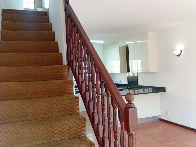Open plan living area featuring a carpeted staircase with wooden balustrade, leading to a kitchen with granite countertops and white cabinetry.
