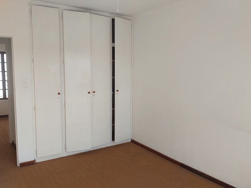 An empty bedroom featuring built-in cupboards, carpeted flooring, and neutral walls, offering a blank canvas for potential updates.