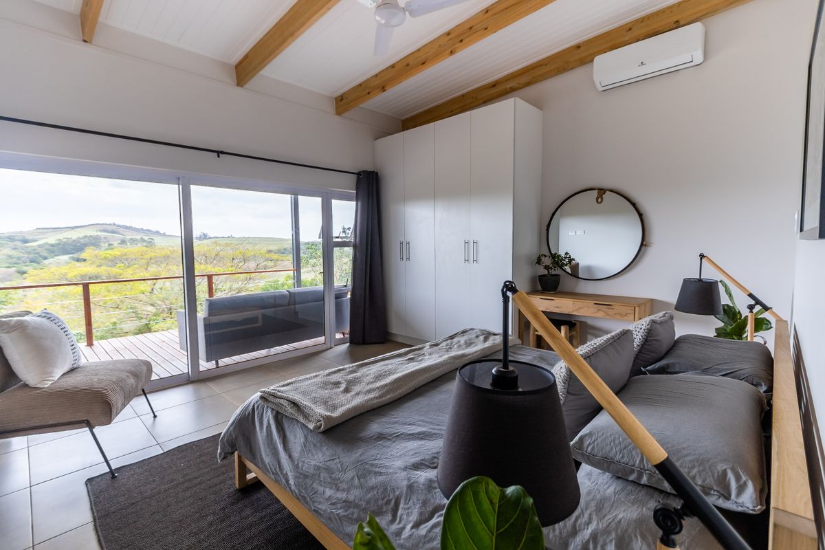 Spacious bedroom featuring exposed timber ceiling beams, built-in wardrobes, split-system air conditioning, and large sliding glass doors opening onto a scenic balcony.