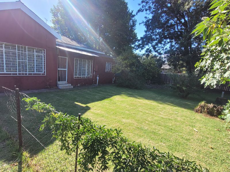 A view of the rear garden and the back facade of the house, featuring a lawn, wire fencing, and security bars on the windows.