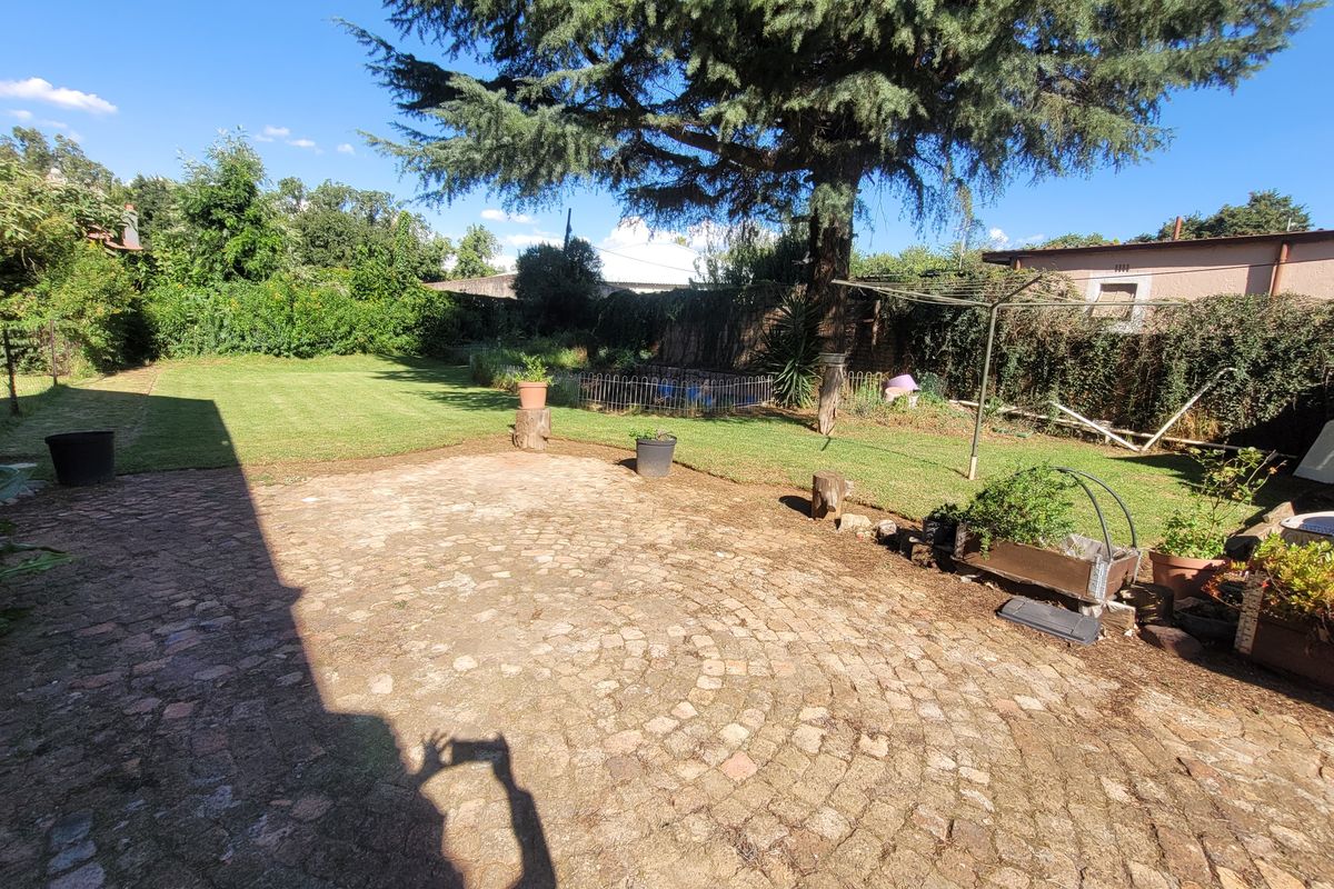 A spacious rear garden featuring a circular cobblestone patio, established lawn, and mature trees, providing a private outdoor area.