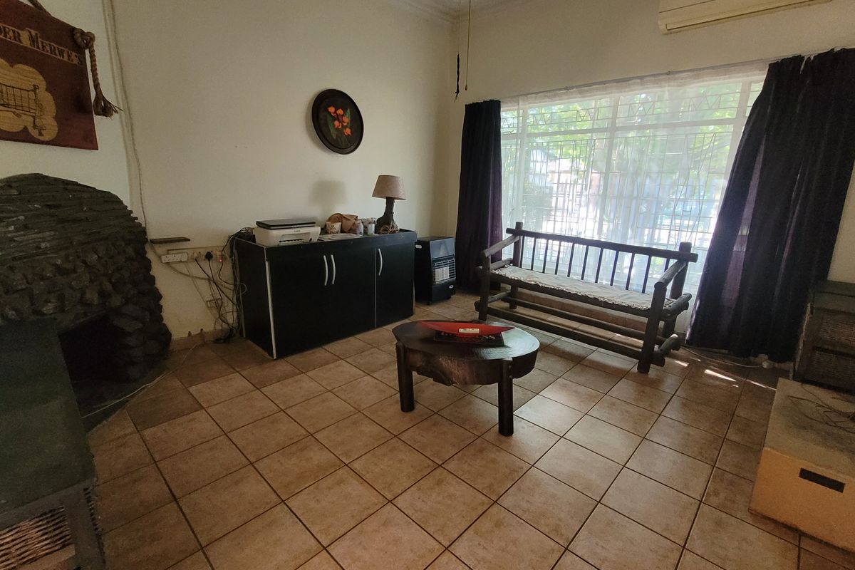 A living room featuring tiled flooring, a stone fireplace, and a large window with security bars, providing a functional and comfortable living space.