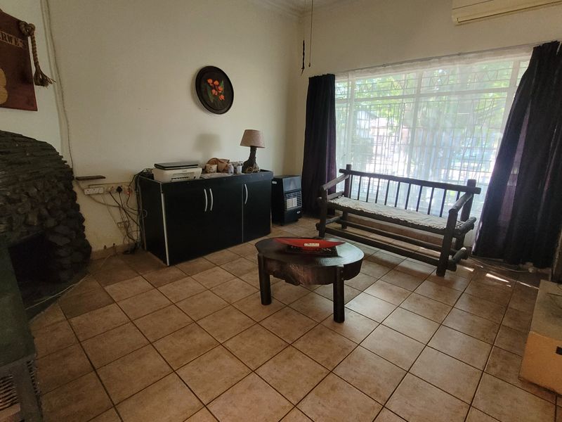 A living room featuring tiled flooring, a stone fireplace, and a large window with security bars, providing a functional and comfortable living space.