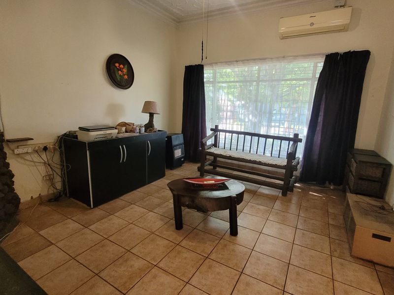 A living room featuring tiled flooring, a stone fireplace, and a wall-mounted air conditioning unit, with large windows providing natural light.