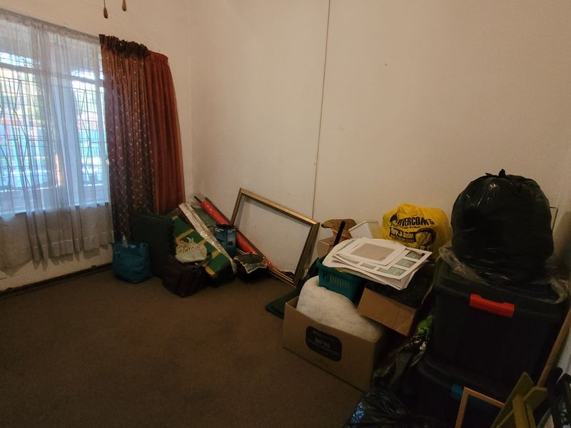 A bedroom space featuring carpeted flooring and a window with security bars, currently used for storage.