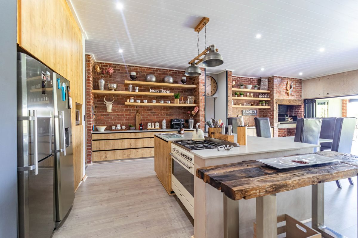 Modern open-plan kitchen featuring exposed brick walls, timber shelving, a central island with a gas hob, and a built-in fireplace.
