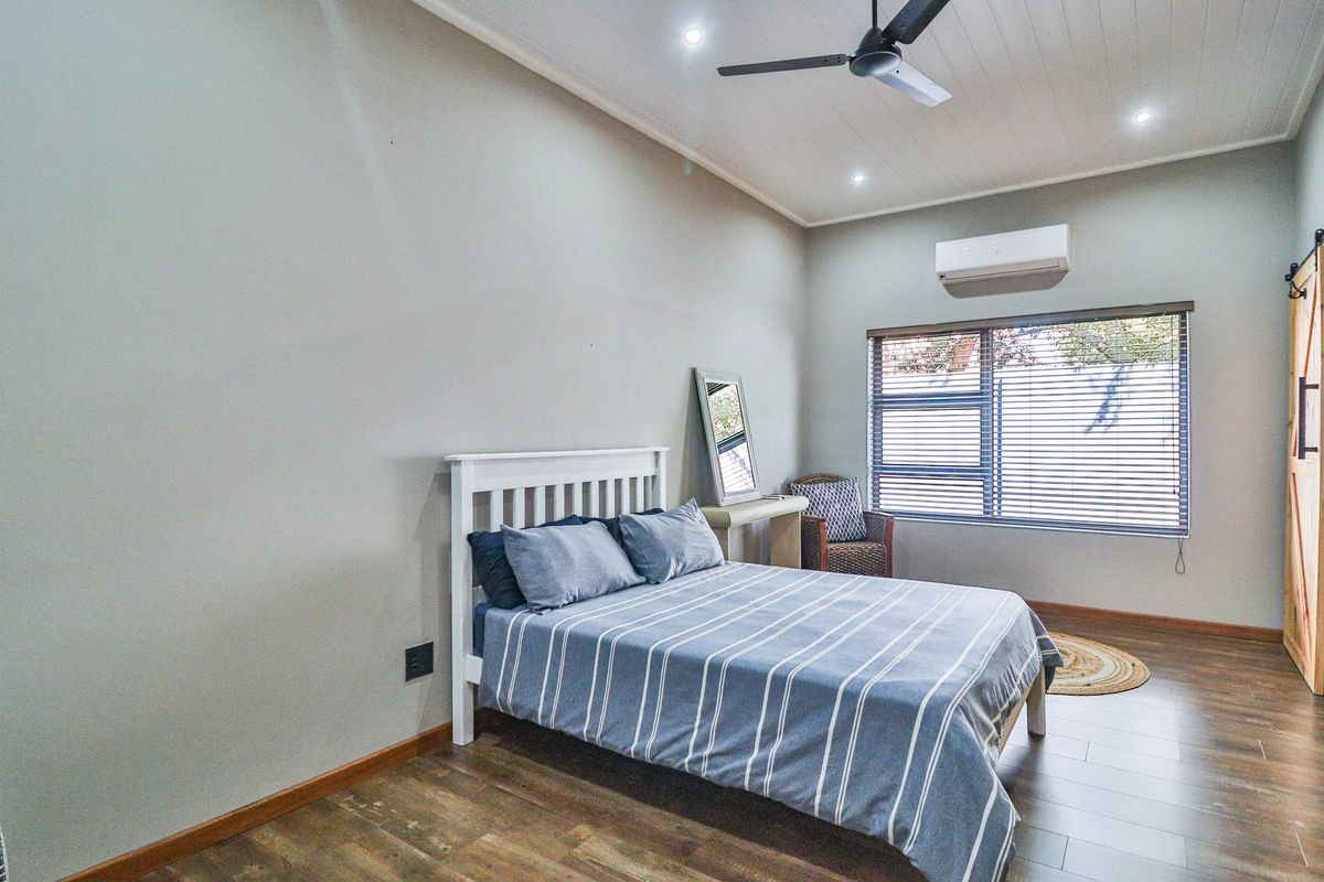 A well-maintained bedroom featuring timber-look flooring, a ceiling fan, split-system air conditioning, and a sliding barn door.