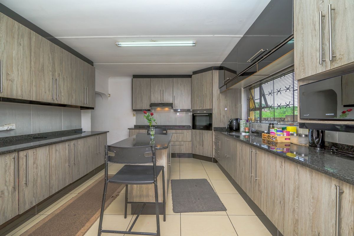 A functional kitchen featuring wood-grain cabinetry, dark granite countertops, a central island, and built-in oven and extractor fan.