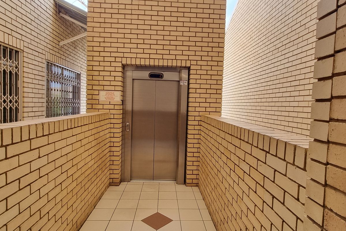 Exterior view of an apartment building corridor featuring a functional elevator, brick masonry walls, and secure metal gates.