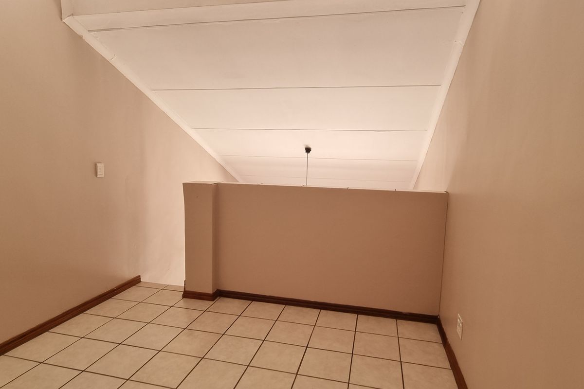 An empty loft-style bedroom featuring tiled flooring and a sloped ceiling, offering a versatile space ready for customization.