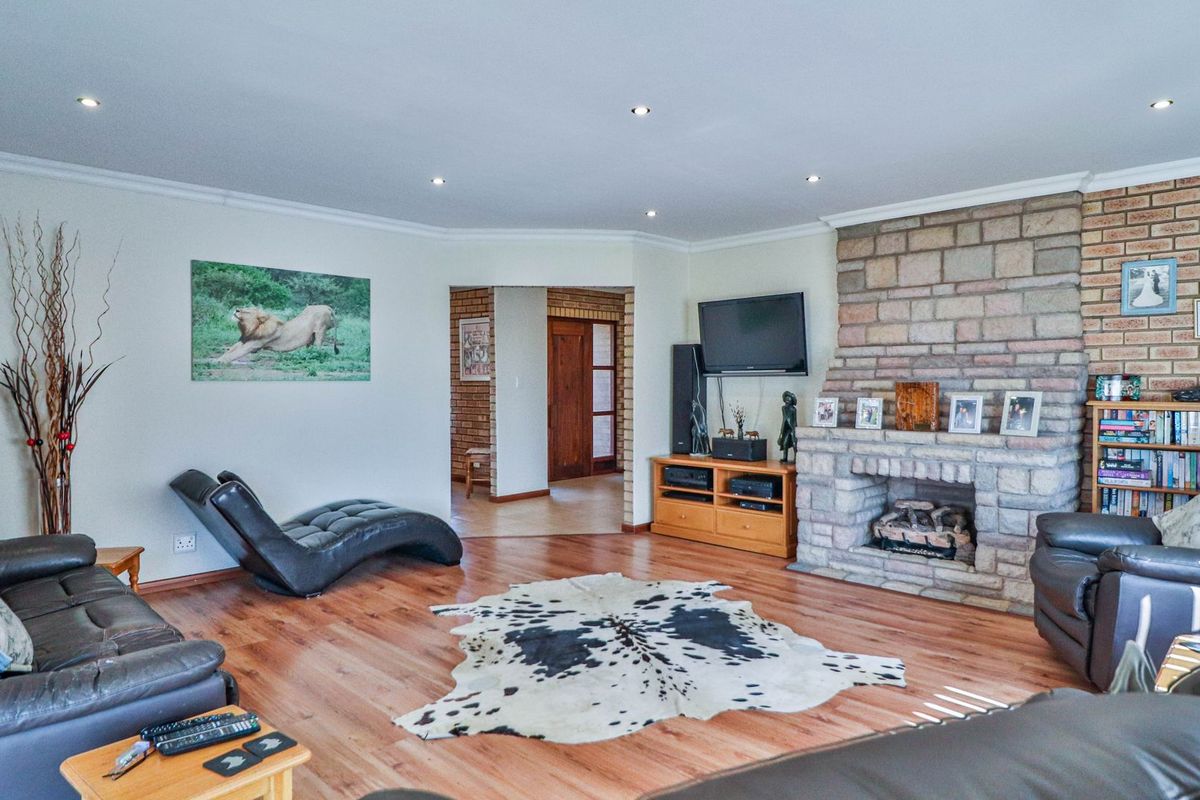 Spacious living room featuring a prominent stone fireplace, laminate flooring, and recessed downlighting, creating a warm and inviting atmosphere.