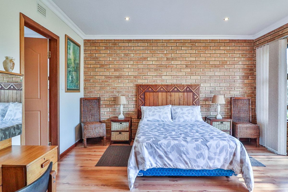 A well-maintained bedroom featuring an exposed brick accent wall, laminate flooring, and direct access to the outdoors via a sliding glass door.