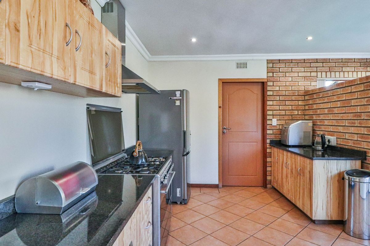 A functional kitchen featuring granite countertops, wooden cabinetry, a gas stove with extractor fan, and a distinctive exposed brick feature wall.