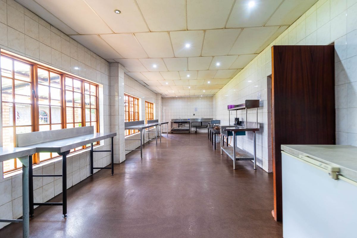 A spacious commercial-style kitchen featuring tiled walls, stainless steel prep surfaces, and multiple windows, suitable for high-volume food preparation or catering operations.