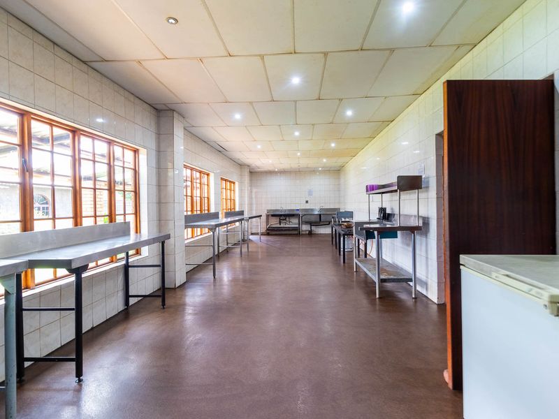 A spacious commercial-style kitchen featuring tiled walls, stainless steel prep surfaces, and multiple windows, suitable for high-volume food preparation or catering operations.