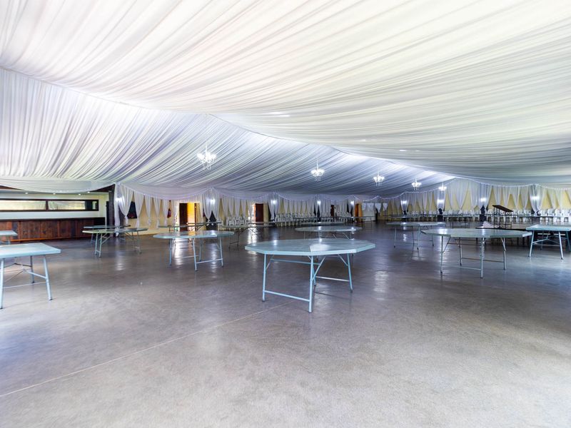 Spacious event hall featuring a draped ceiling, polished concrete floors, integrated bar area, and decorative chandeliers, suitable for large gatherings and functions.