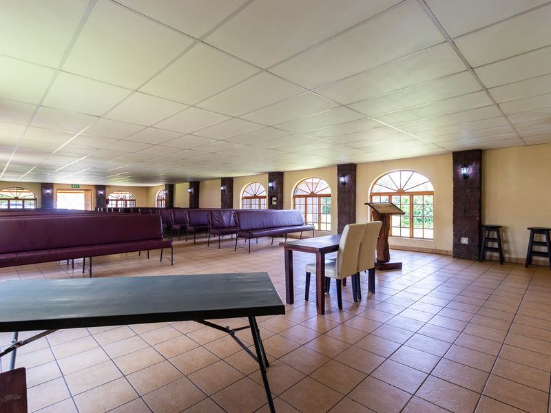 A spacious multi-purpose hall featuring tiled flooring, arched windows, and stone-clad pillars, suitable for events or community gatherings.