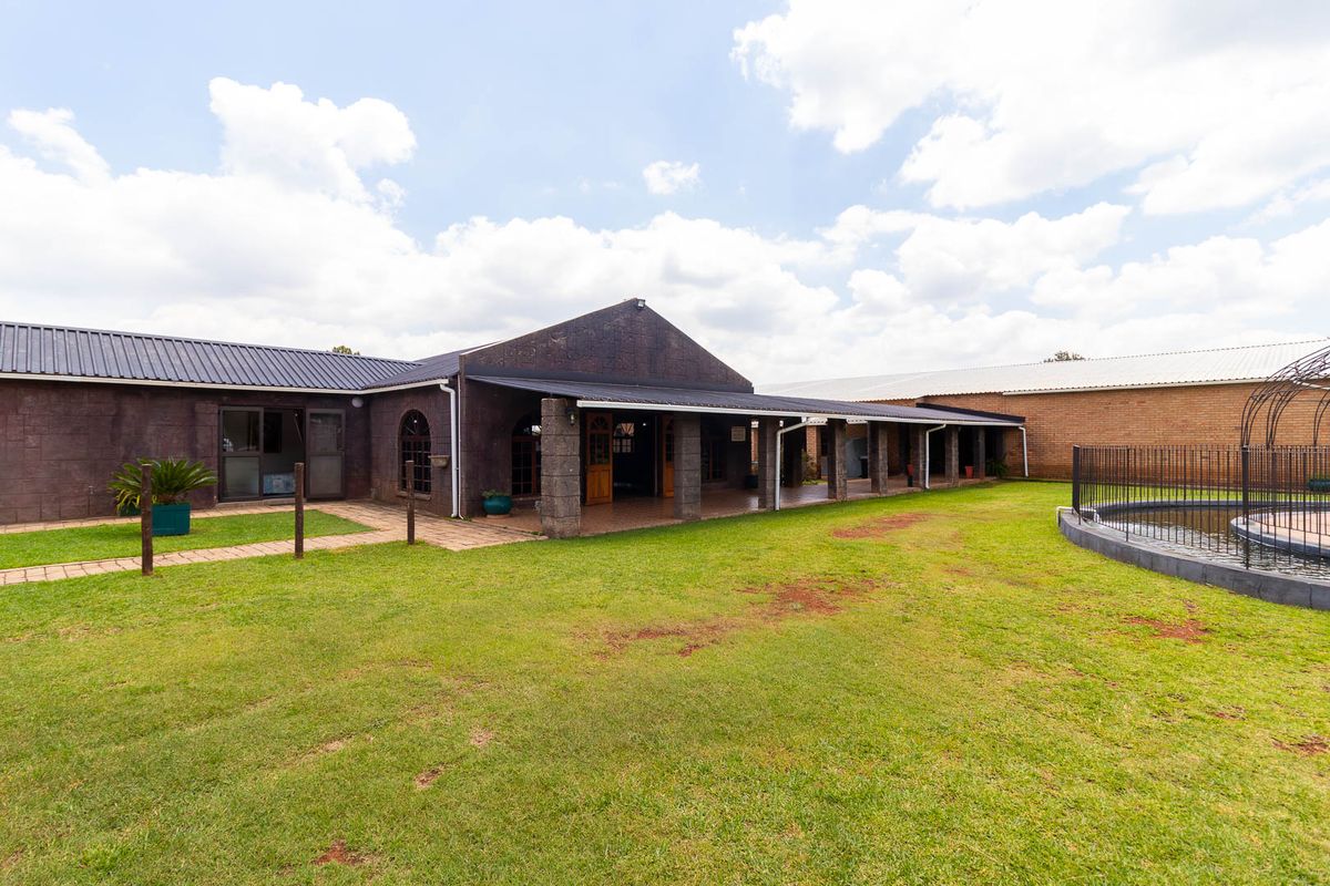 Rear view of the farm property featuring a spacious covered patio, stone-clad exterior, and a fenced swimming pool set within a large lawn area.