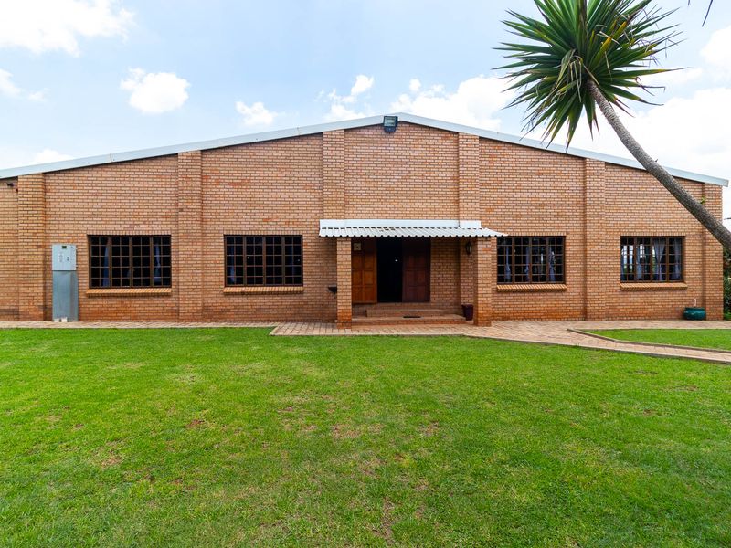 A well-maintained face brick farm building featuring a pitched metal roof, timber-framed windows, and a paved entrance walkway set against a manicured lawn.