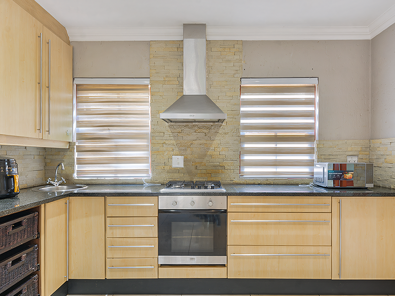 A functional kitchen featuring light wood cabinetry, granite countertops, a stone-clad backsplash, and integrated stainless steel appliances including an oven and extractor fan.