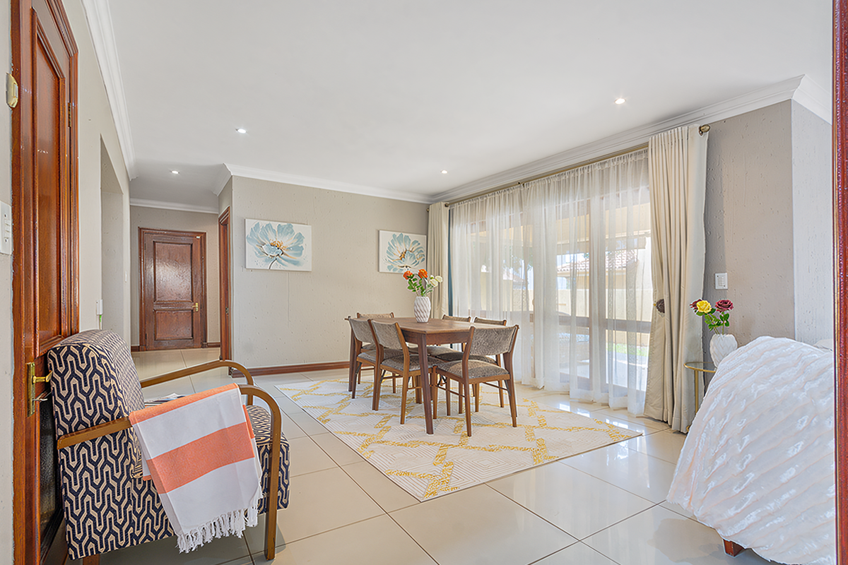 A bright and spacious living area featuring large sliding glass doors, neutral tiled flooring, and elegant cornicing, creating a welcoming and well-maintained atmosphere.