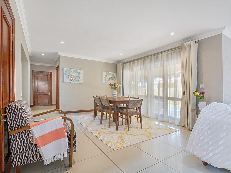 A bright and spacious living area featuring large sliding glass doors, neutral tiled flooring, and elegant cornicing, creating a welcoming and well-maintained atmosphere.
