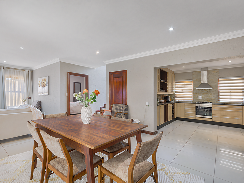 Spacious open-plan living and dining area featuring a modern kitchen with built-in appliances, stone splashback, and sleek porcelain floor tiles throughout.