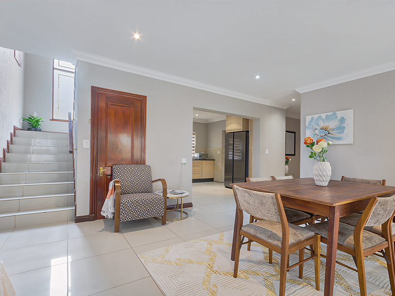 An open-plan dining area featuring tiled flooring, recessed lighting, and a staircase, with a view into the adjacent kitchen space.