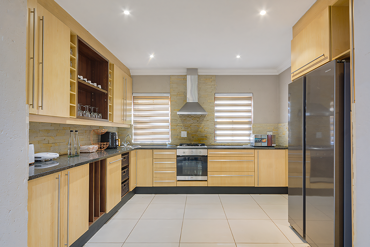 Modern kitchen featuring light wood cabinetry, granite countertops, stone cladding backsplash, and integrated stainless steel appliances, illuminated by recessed downlights.
