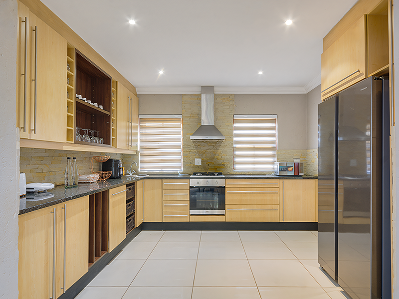 Modern kitchen featuring light wood cabinetry, granite countertops, stone cladding backsplash, and integrated stainless steel appliances, illuminated by recessed downlights.
