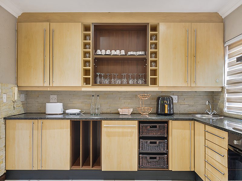 A functional kitchen featuring light wood cabinetry, granite countertops, a stone tile backsplash, and integrated storage solutions including a wine rack.