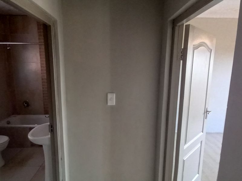 A view of a hallway connecting a bathroom and an adjacent room, featuring standard internal doors and neutral wall finishes.