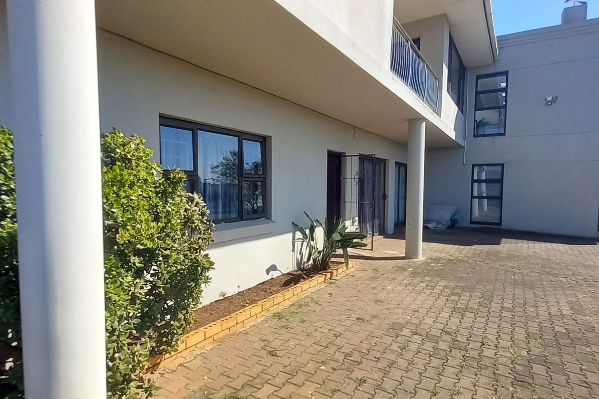 Rear exterior view of the property featuring a paved courtyard, support columns, and a balcony with metal railings.