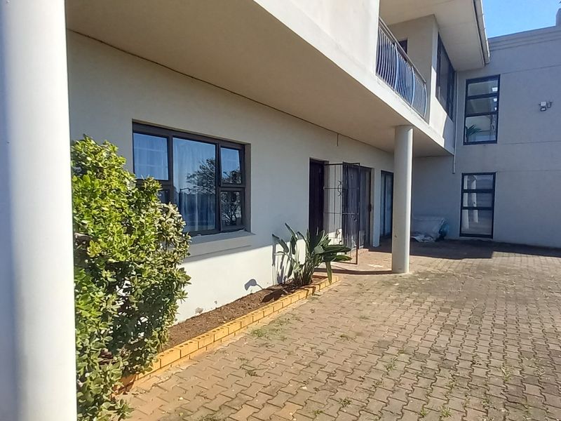 Rear exterior view of the property featuring a paved courtyard, support columns, and a balcony with metal railings.