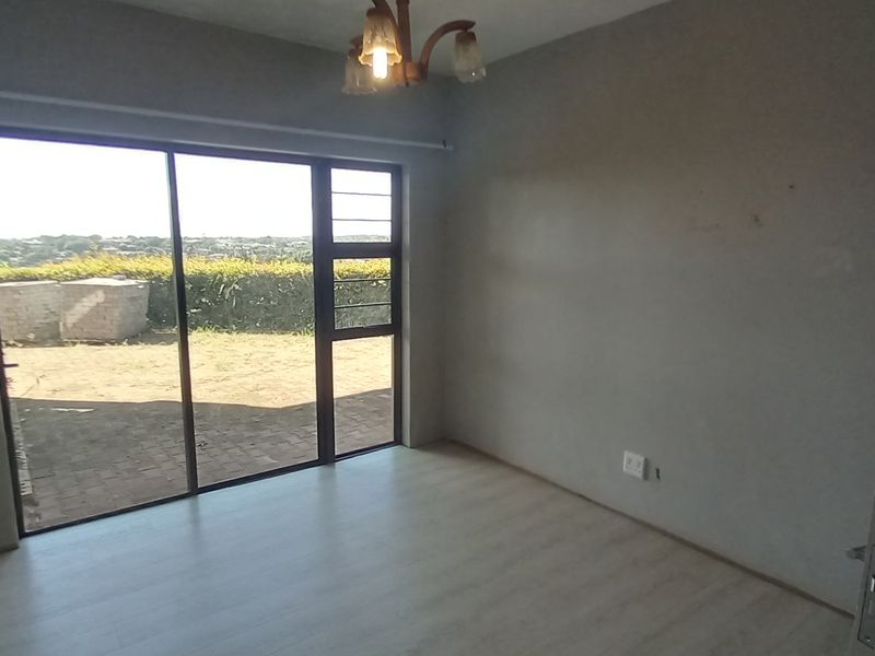 An empty bedroom featuring laminate flooring, a ceiling light fixture, and a large sliding glass door providing access to the exterior.