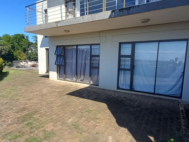 Rear exterior view of the flat featuring a paved patio area, sliding glass doors, and an upper-level balcony with a stainless steel balustrade.