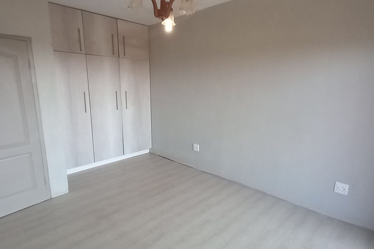A clean, empty bedroom featuring neutral grey walls, light-toned laminate flooring, and ample built-in cupboard storage.