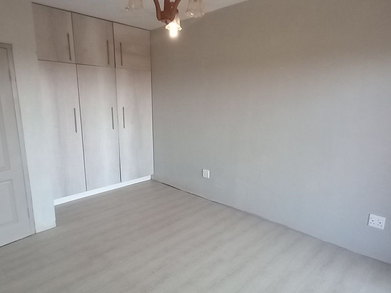 A clean, empty bedroom featuring neutral grey walls, light-toned laminate flooring, and ample built-in cupboard storage.