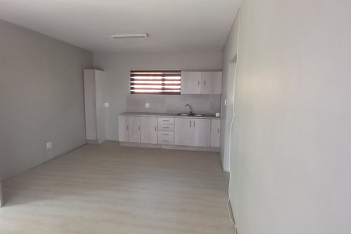 An open-plan living and kitchen area featuring light-toned laminate flooring, neutral walls, and functional kitchen cabinetry with a built-in sink.