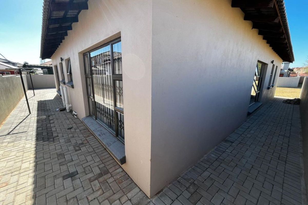 A view of the rear exterior of the house featuring paved walkways, security gates on windows, and a tiled roof.