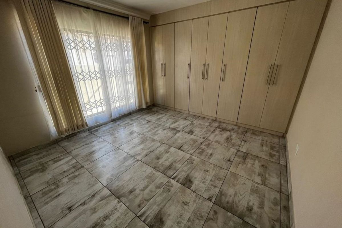 A bright, empty bedroom featuring modern wood-look floor tiles, extensive built-in cabinetry, and a sliding door providing access to the exterior.