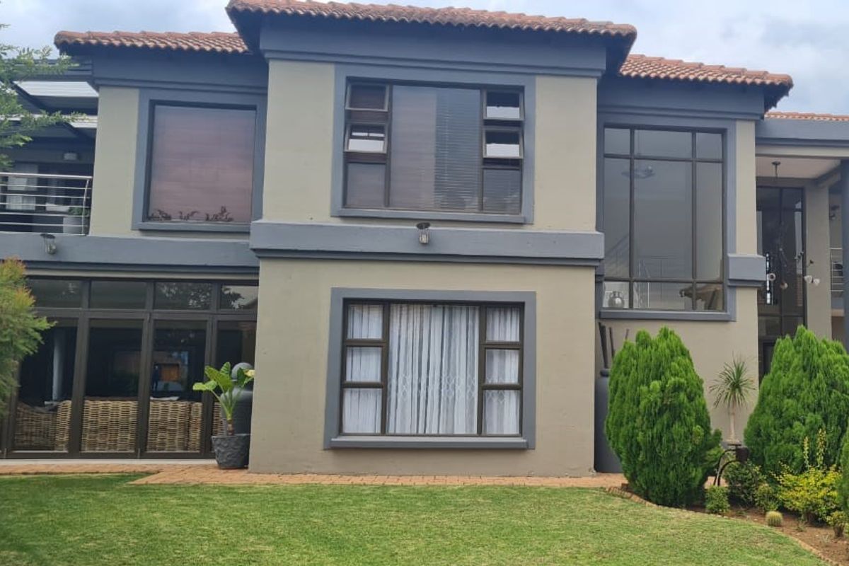 Rear elevation of a two-story house featuring terracotta roof tiles, aluminium framed windows, and a paved patio area overlooking a landscaped garden.
