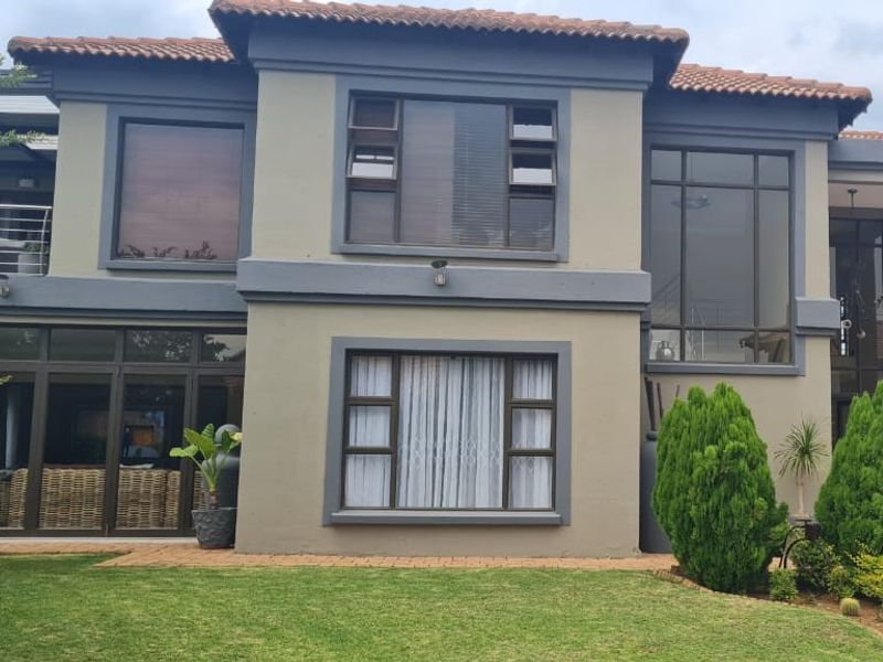 Rear elevation of a two-story house featuring terracotta roof tiles, aluminium framed windows, and a paved patio area overlooking a landscaped garden.