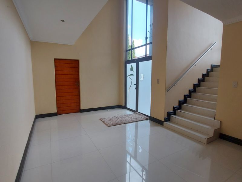Spacious entrance hall featuring high ceilings, large windows, tiled flooring, and a staircase with a metal handrail.