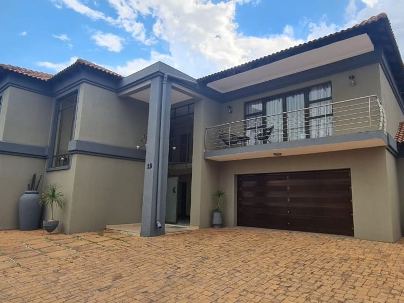 A modern double-story residential property featuring a paved driveway, integrated double garage, and an upper-level balcony with stainless steel balustrades.