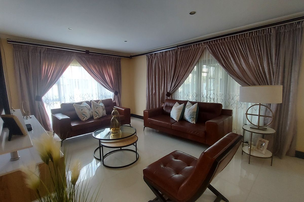 A well-maintained living room featuring polished tiled flooring, recessed downlighting, and large windows dressed with elegant floor-to-ceiling curtains.