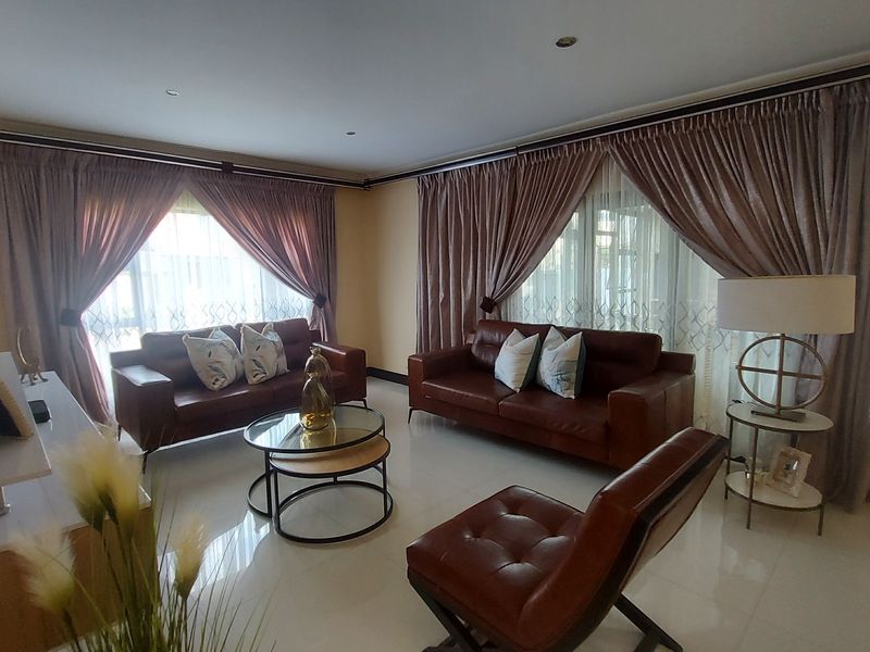 A well-maintained living room featuring polished tiled flooring, recessed downlighting, and large windows dressed with elegant floor-to-ceiling curtains.