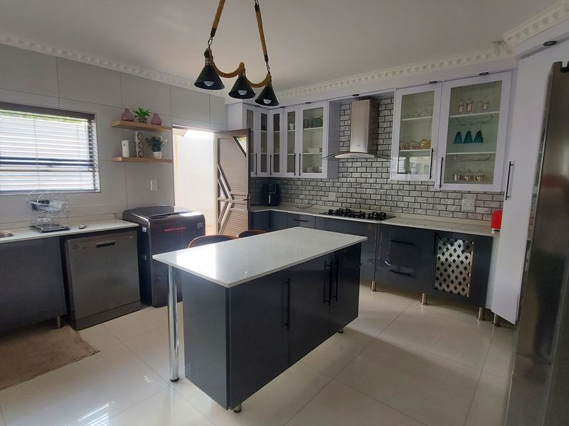 Modern kitchen featuring dark cabinetry, a central island with stone countertop, gas hob, extractor fan, and stylish tiled backsplash with ample storage space.