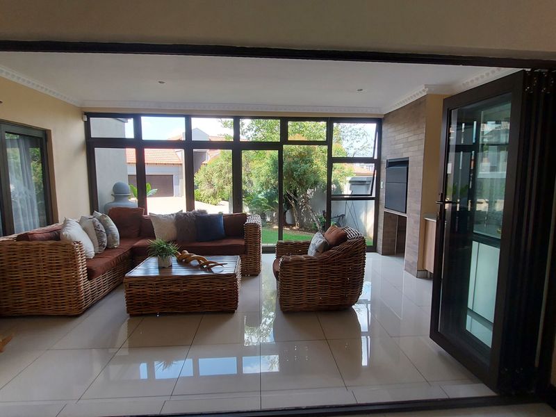 Spacious enclosed patio featuring large aluminium stack doors, tiled flooring, and a built-in braai, creating a seamless transition to the garden.